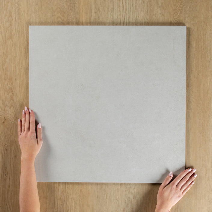 Person holding a light gray square tile on a wooden surface