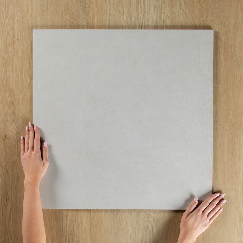 Person holding a light gray square tile on a wooden surface